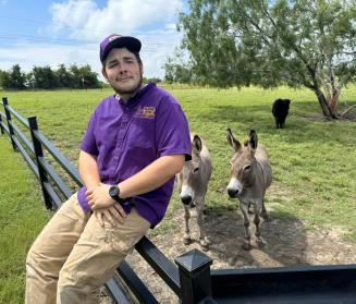 Brett seated on a fence in front of a pair of donkeys